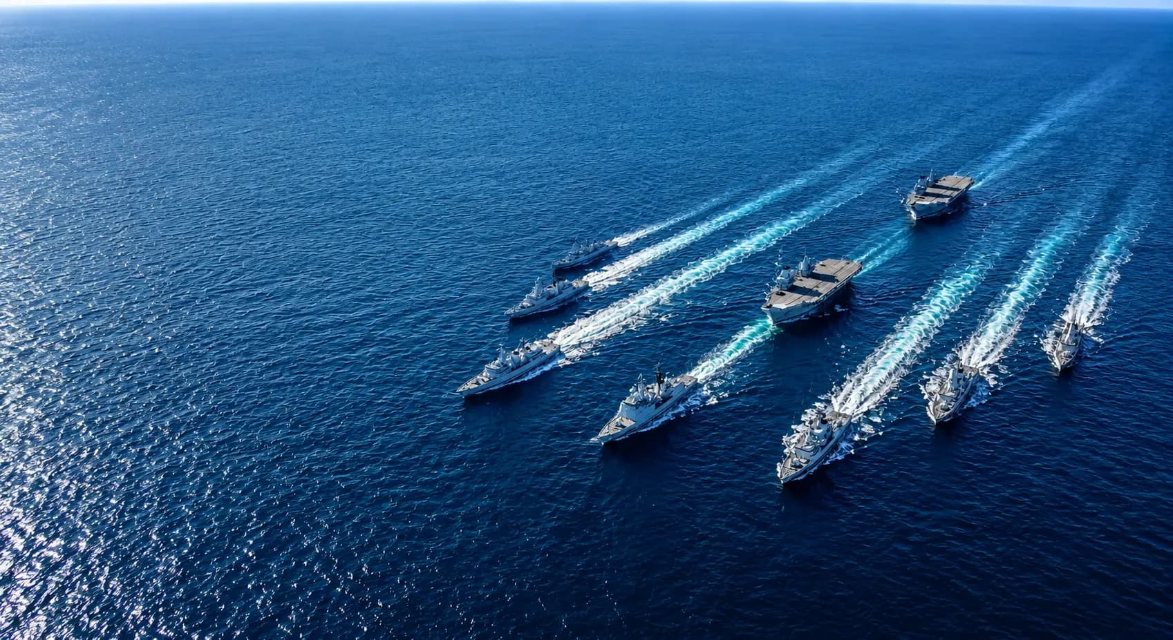 Aerial view of a naval fleet sailing in formation across deep blue ocean water
